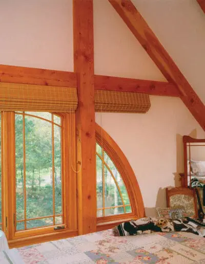 Timber frame master bedroom with large rounded windows and timber accents.