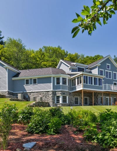 Exterior of large blue-grey home with white trim and stone foundation.