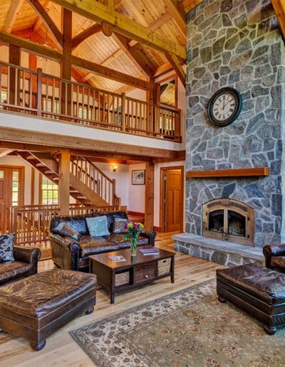 Timber frame great room with large stone fireplace and distressed leather furniture.